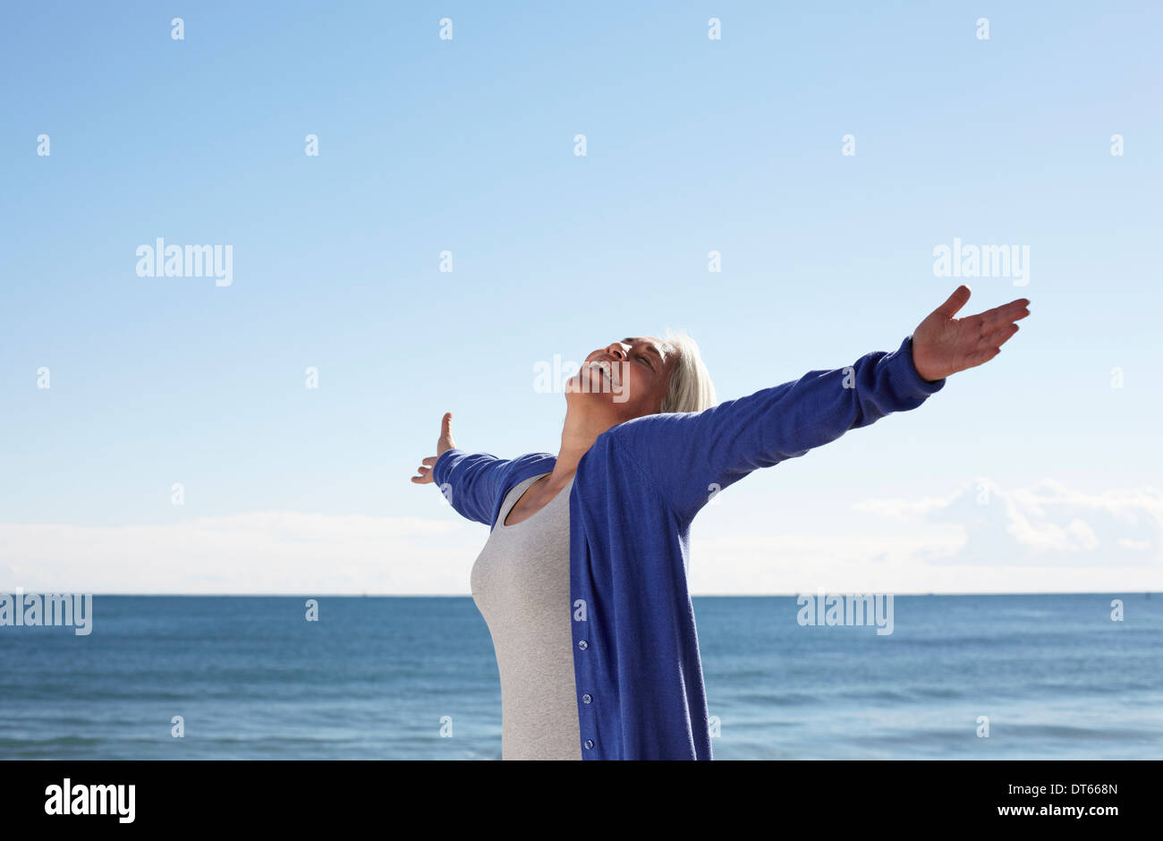 Mature woman on beach with arms outspread Stock Photo