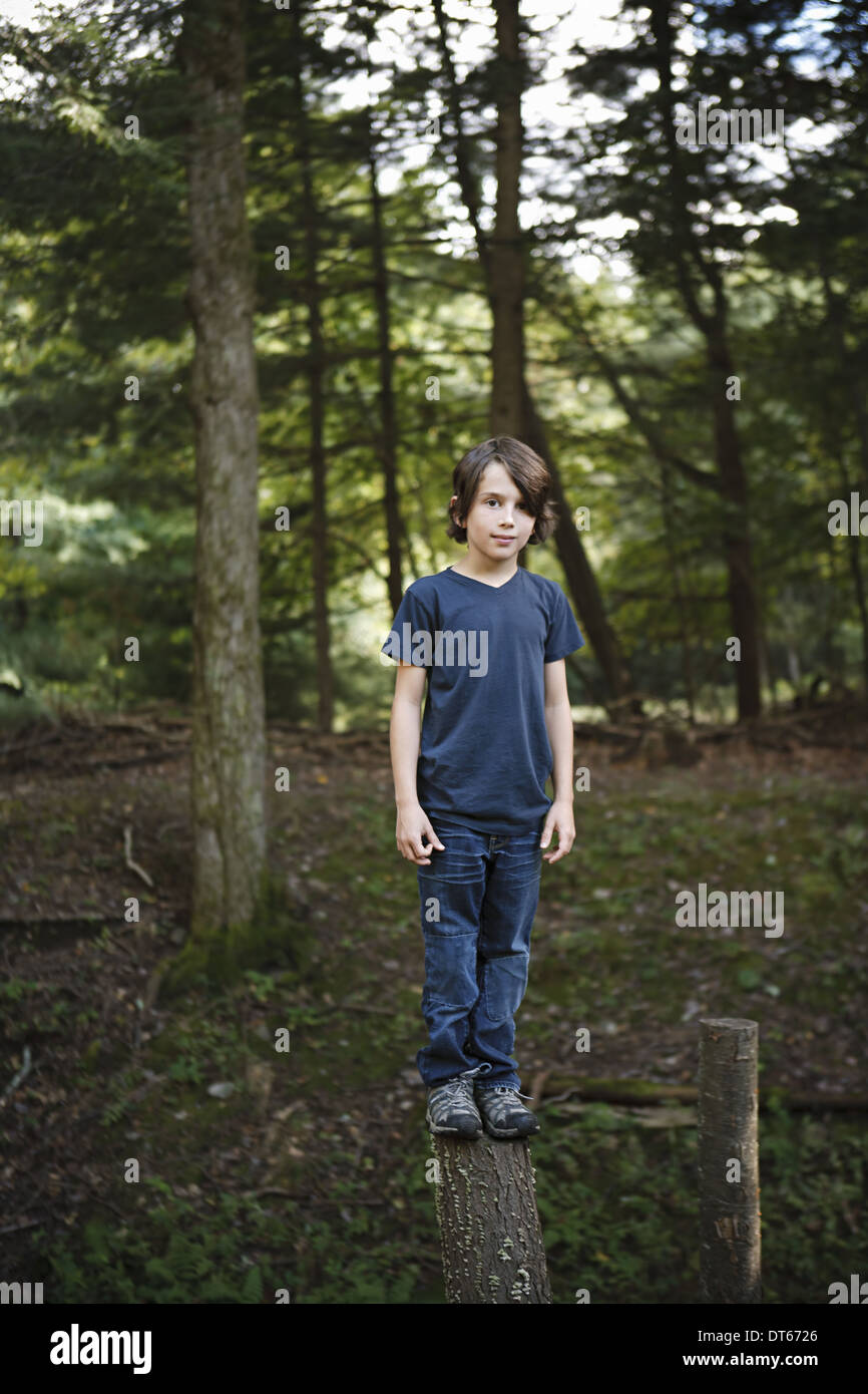 A boy standing on a narrow tree trunk, balancing and walking the plank. Stock Photo