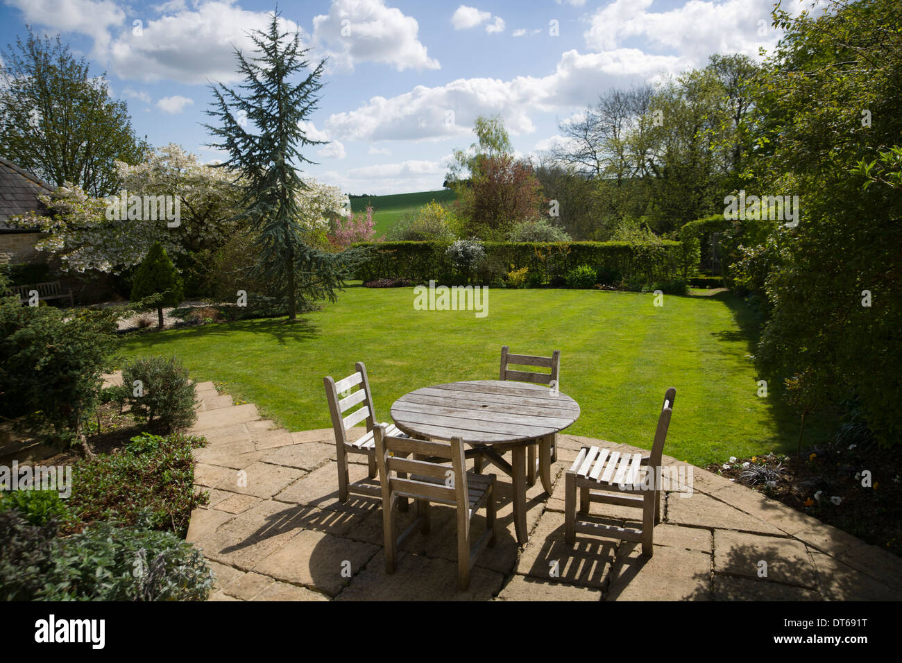 UK gardens. Wooden table and chairs on a patio in a mature garden. Stock Photo