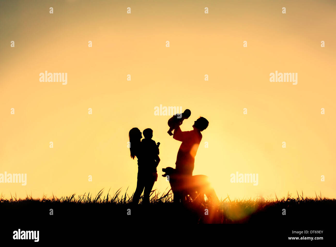 A silhouette of a happy family of four people, mother, father, baby, and child, and their dog in front of a sunsetting sky, Stock Photo