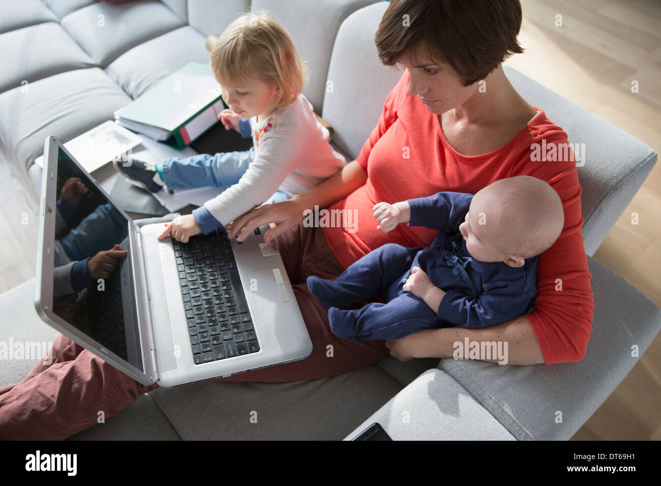Mother, baby boy and female toddler using laptop on sofa Stock Photo