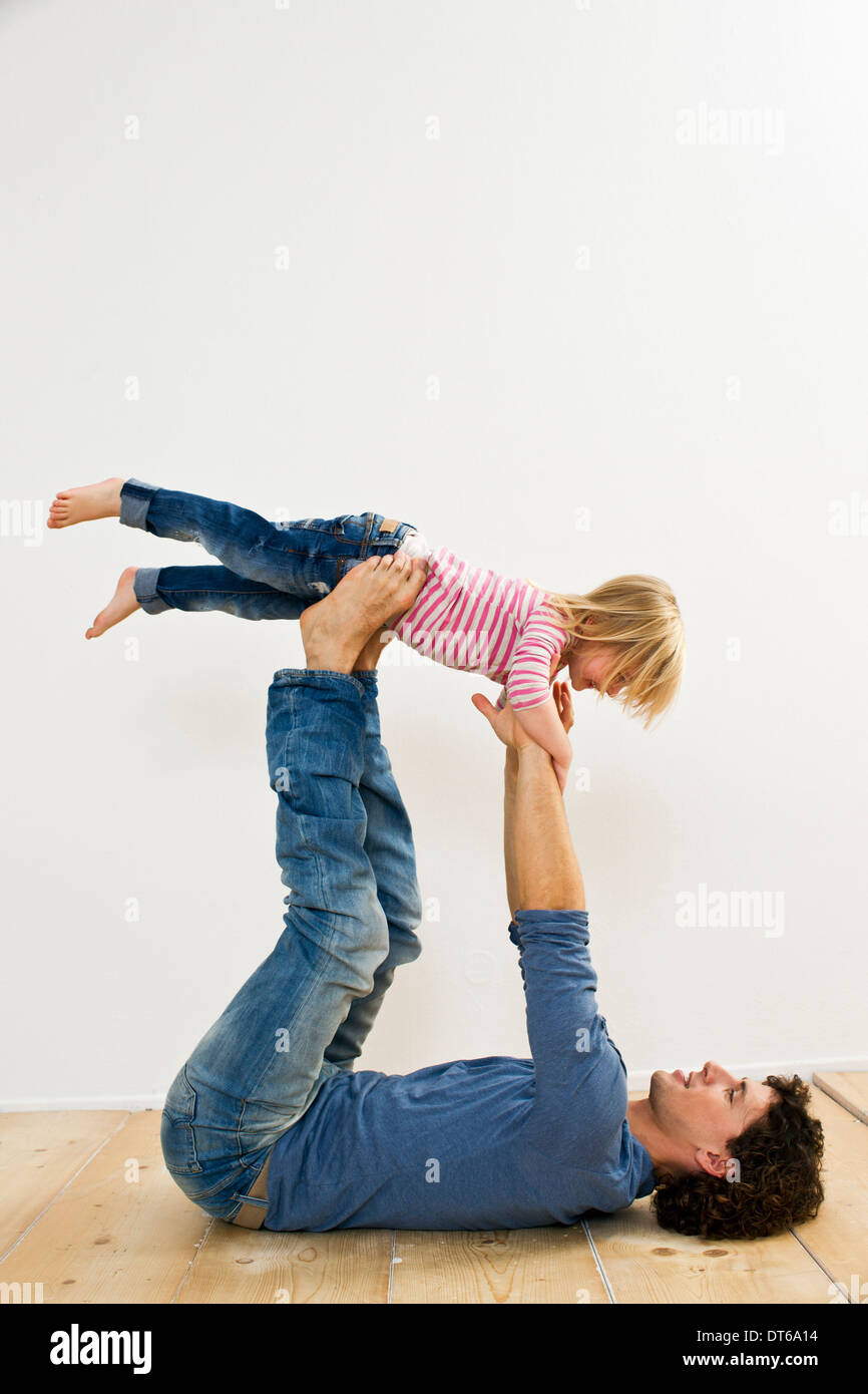 Studio shot of father lifting up daughter whilst lying on back Stock Photo