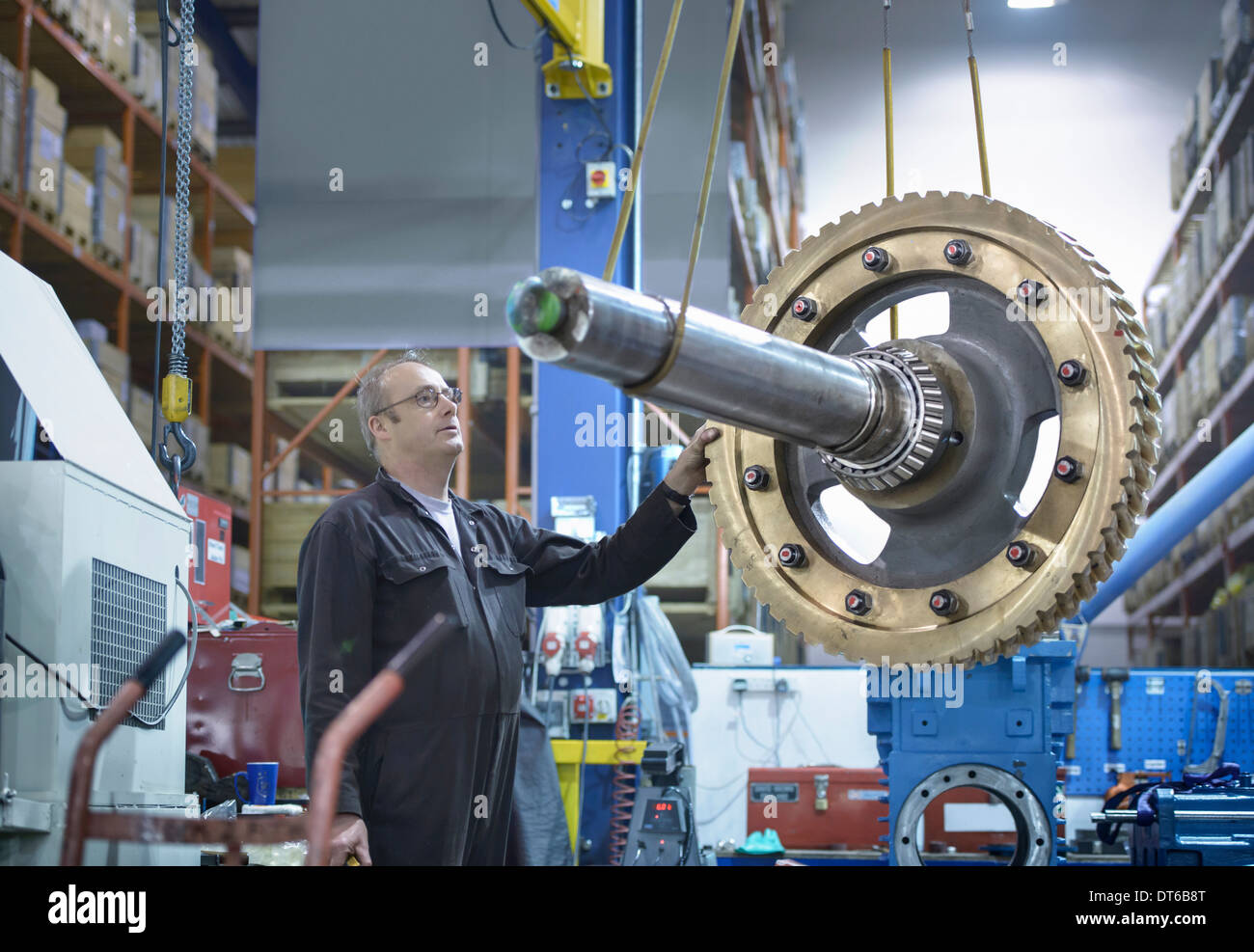 Engineer using crane to move large gear wheel in engineering factory