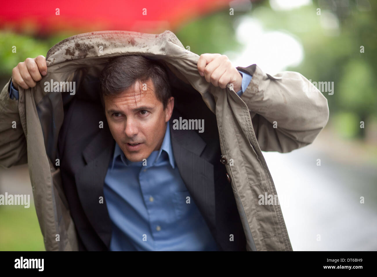 Businessman holding up raincoat to shelter from rain Stock Photo
