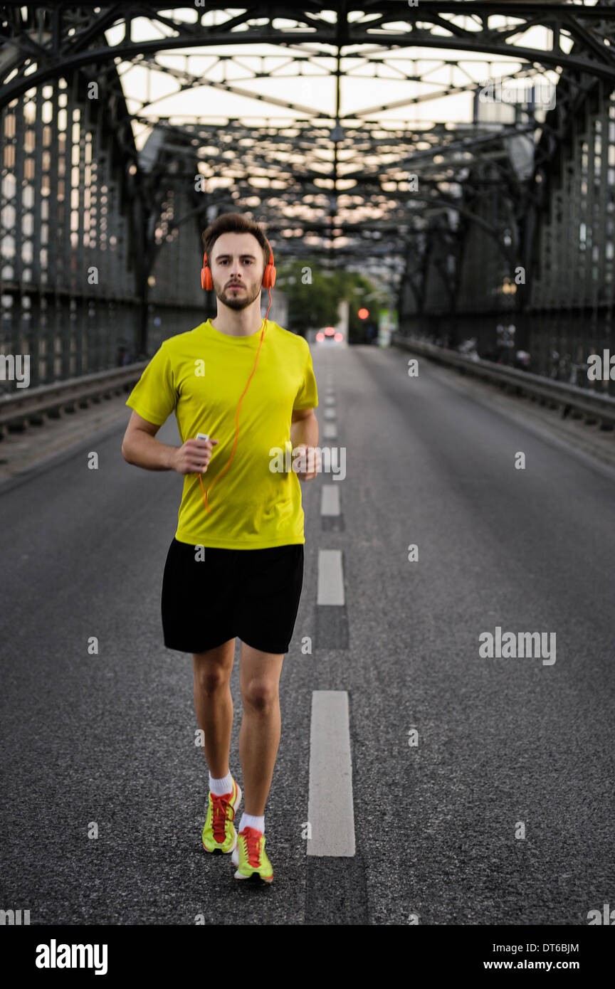Young male athlete running on bridge wearing headphones Stock Photo
