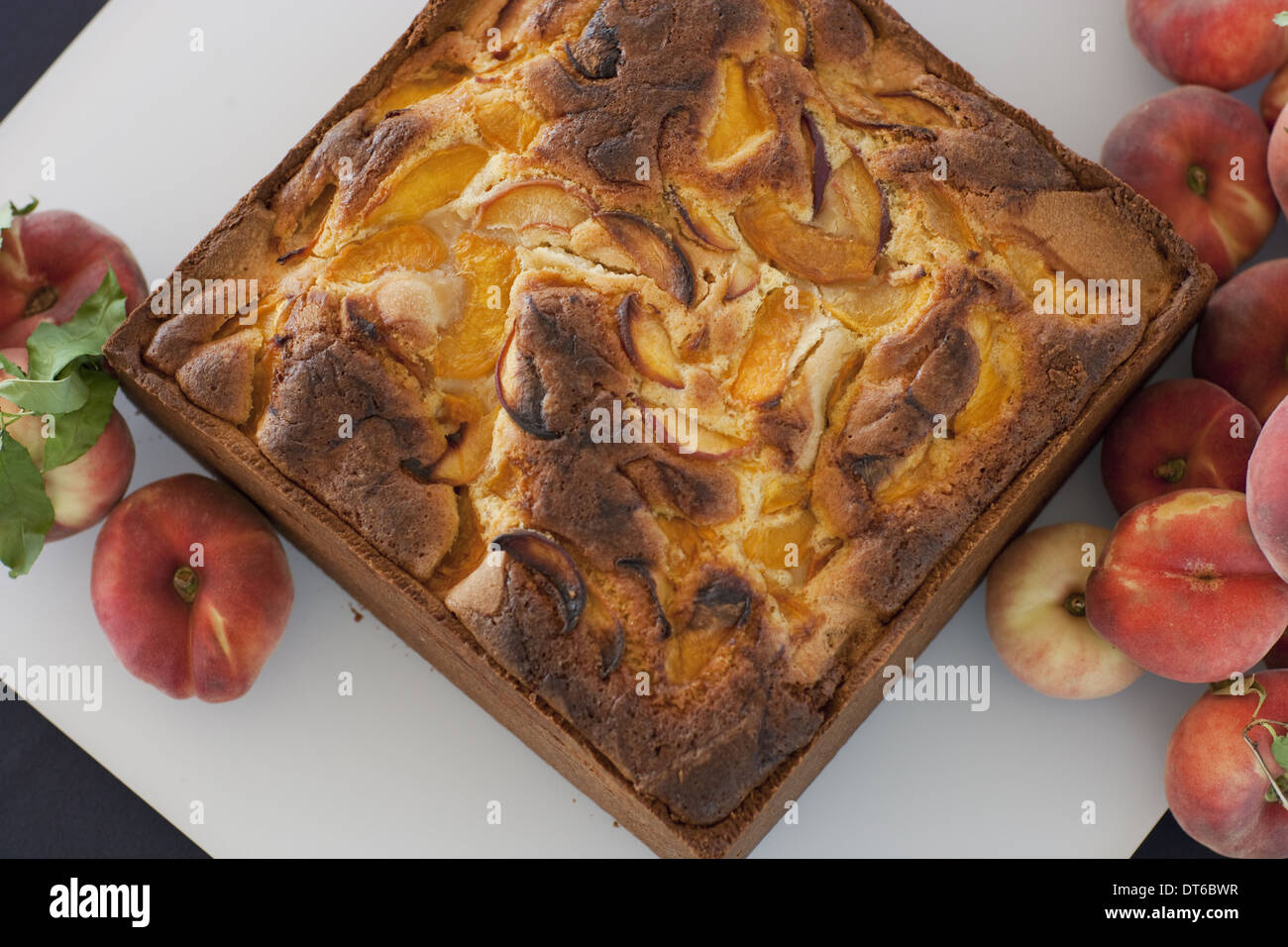 A square baked peach cake on a board with fresh peaches. Fruits. Organic fresh food on a farm stand. Stock Photo