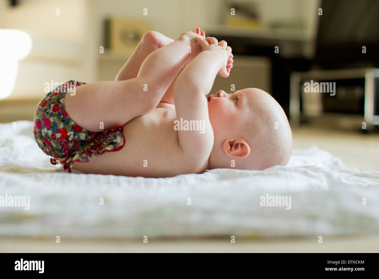 Baby girl lying on back playing with feet Stock Photo