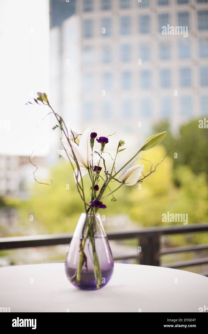 A table on a terrace in the city. A vase of flowers. Small purple flowers, and white lily and orchid blooms. Stock Photo