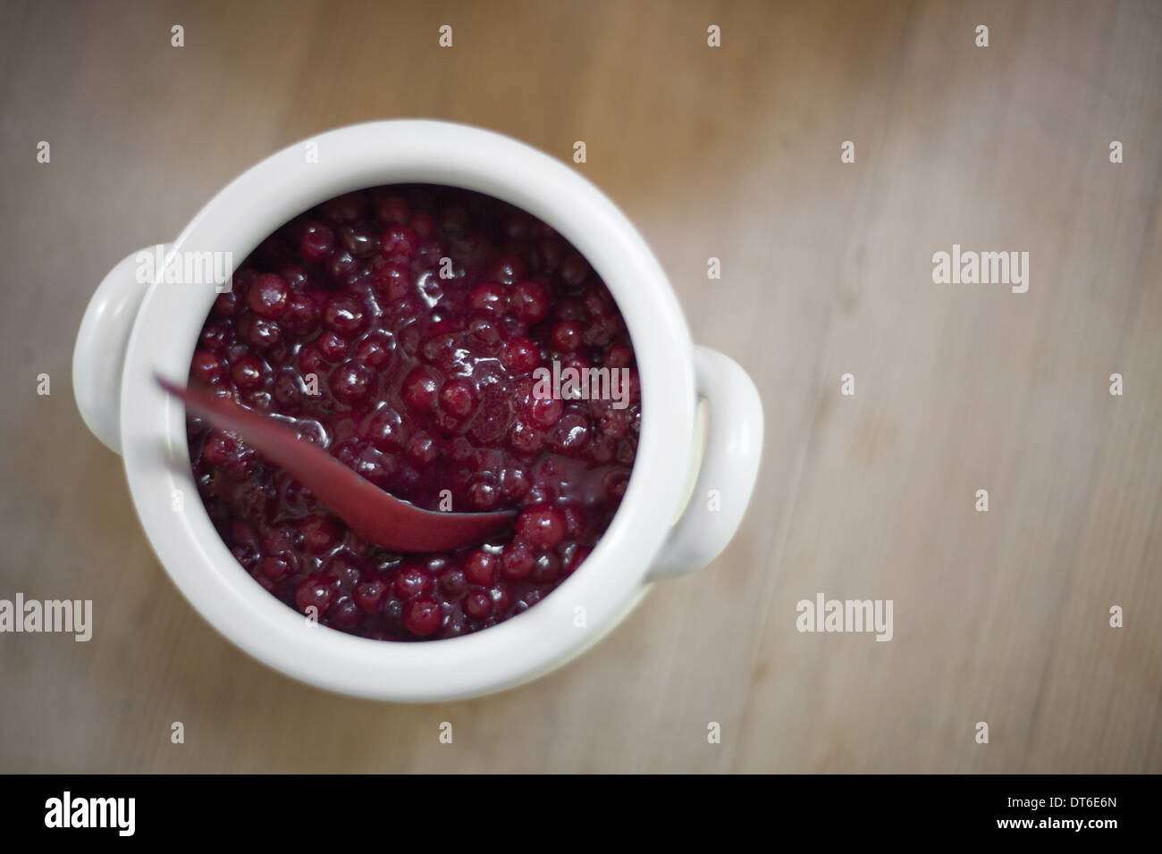 A white pottery bowl, full of fresh cranberries with a matching spoon. A relish or sauce. Stock Photo