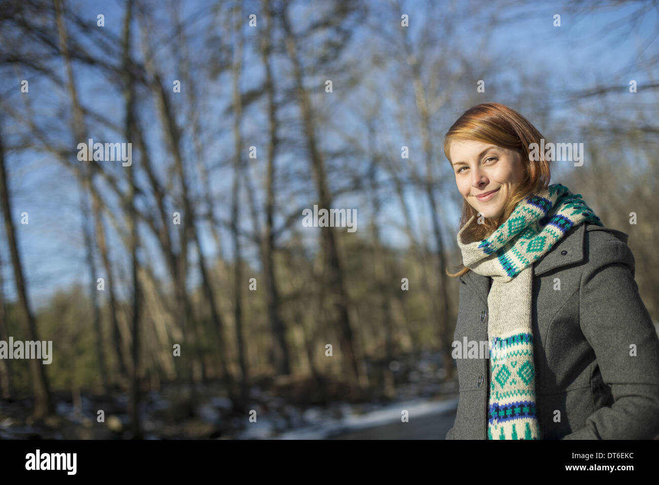 A young woman in a woodland on a winter day.  Wearing a bright knitted patterned scarf. Stock Photo