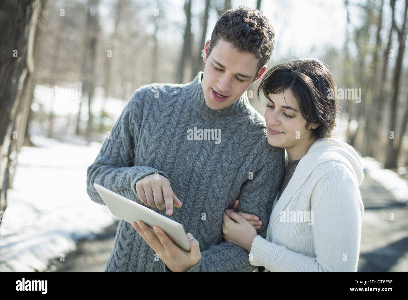 A couple looking at a computer tablet. Standing close together on a winter day in the woods. Stock Photo
