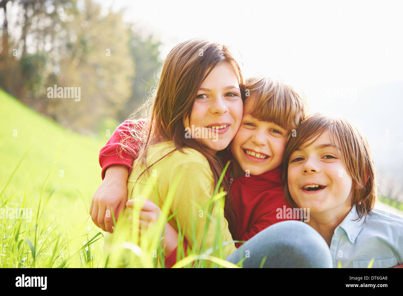 Sister and younger brothers sitting in grassy field Stock Photo