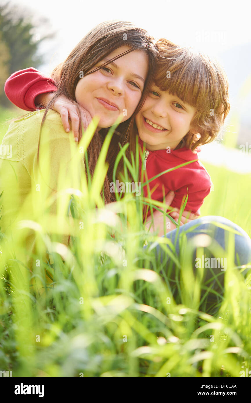 Sister and younger brother sitting in grassy field Stock Photo