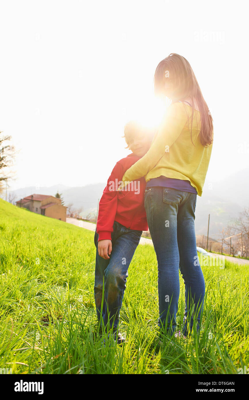 Young boy and older sister in grassy field Stock Photo