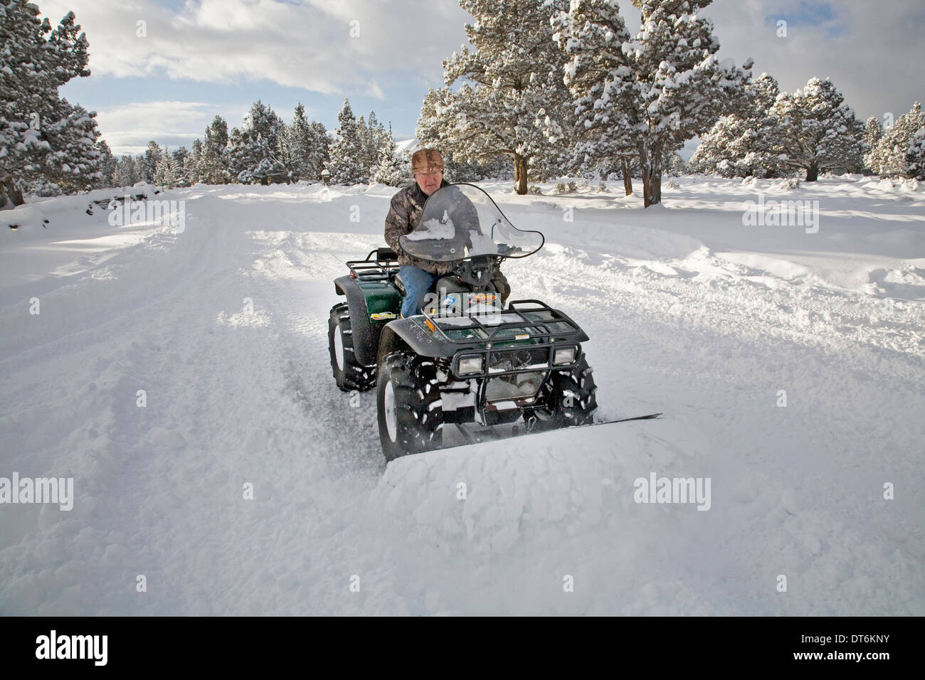 A senior citizen plows snow with an ATV, all terrain vehicle, after a major snow storm in central Oregon. Stock Photo