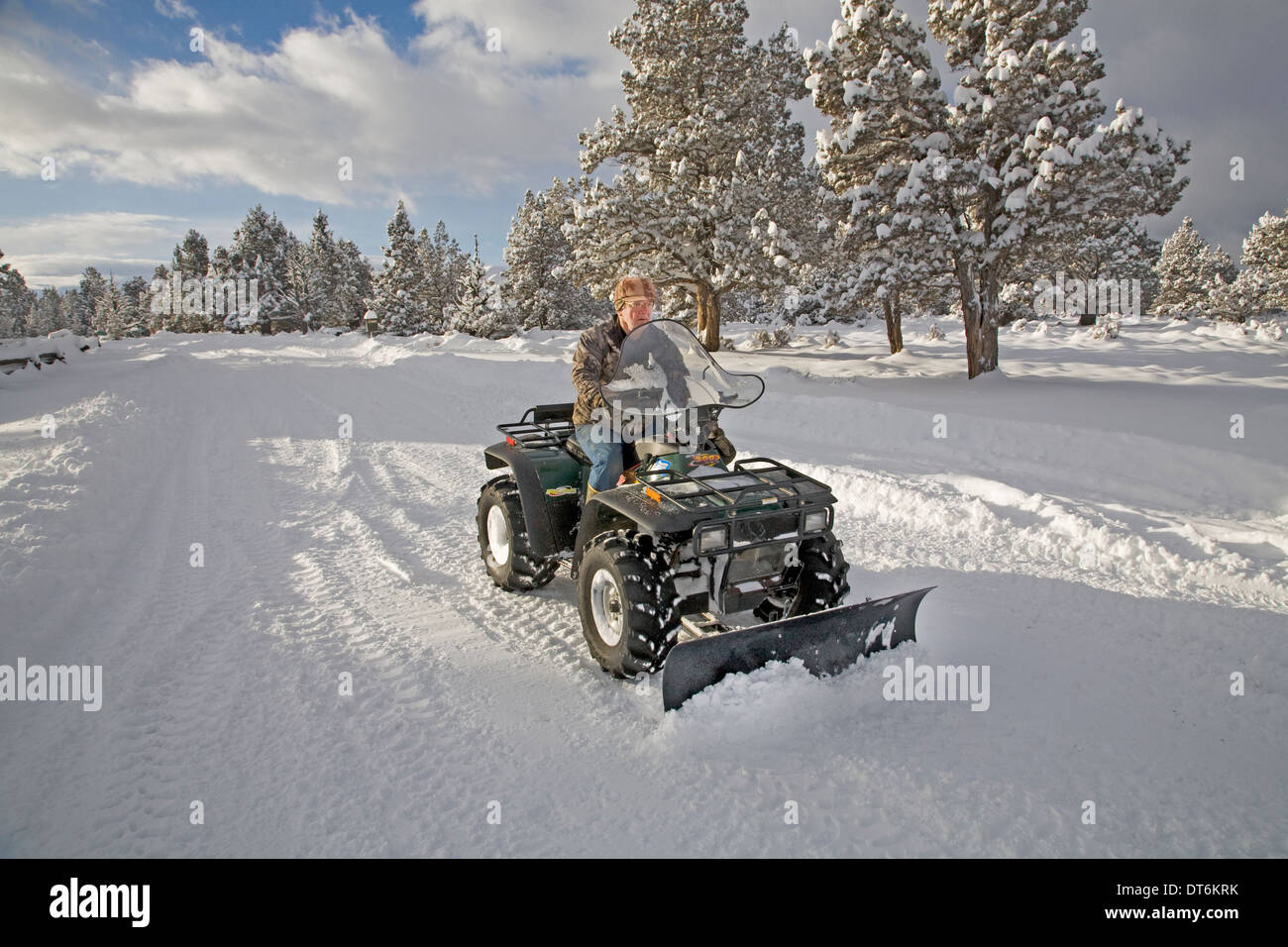 A senior citizen plows snow with an ATV, all terrain vehicle, after a