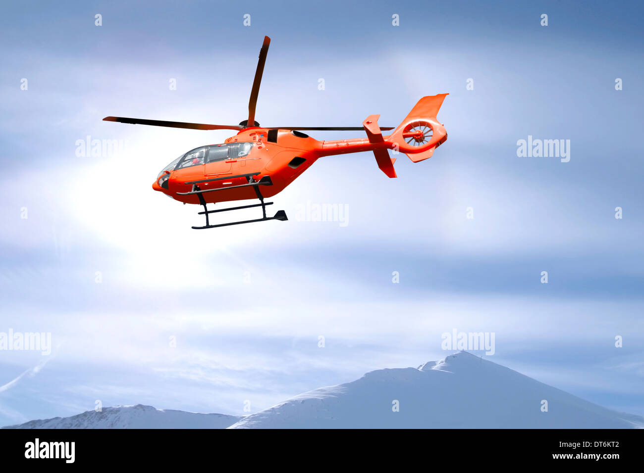 Red helicopter flies over snow capped mountain summits Stock Photo