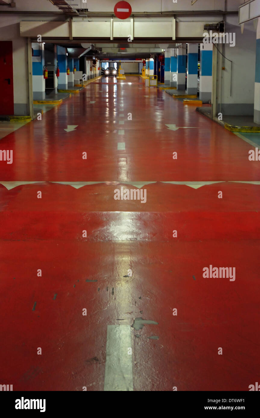 Underground multi-storey car park interior. Red driveway and approaching car. Stock Photo