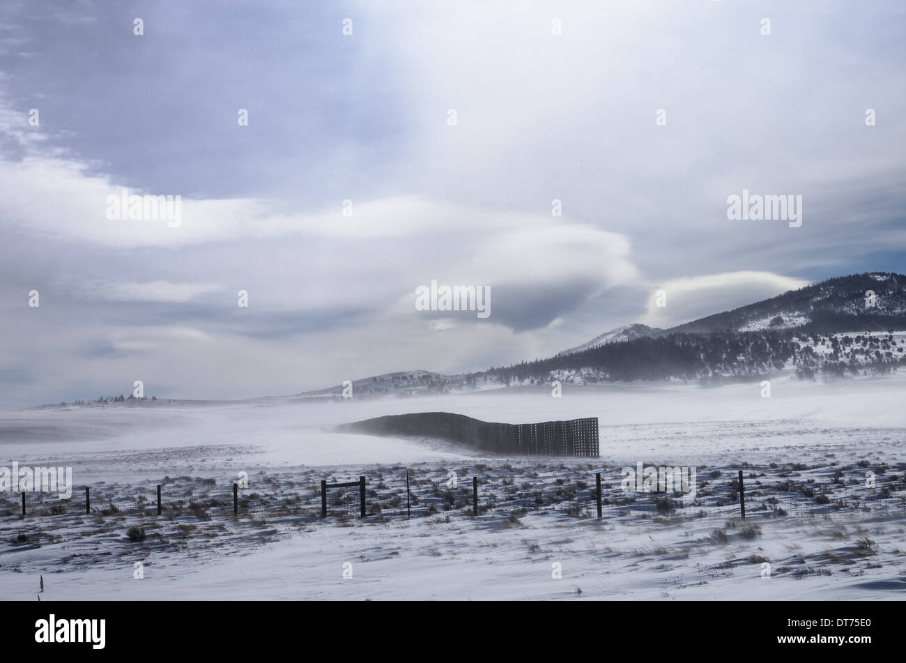 a snow fence helps to trap blowing snow along a highway in Wyoming Stock Photo