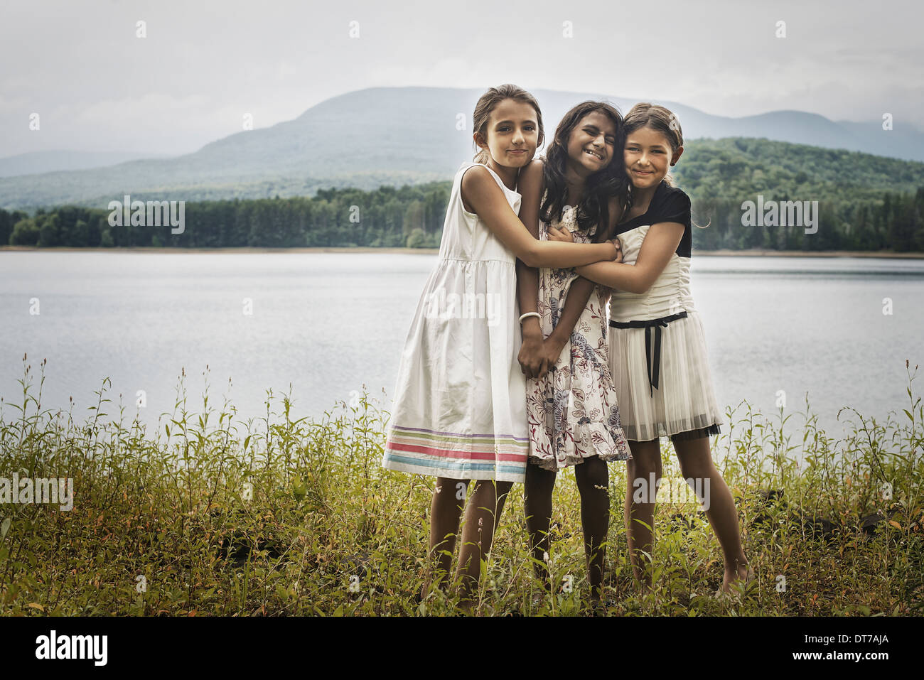 Three young girls standing by the side of a lake hugging each other Woodstock New York USA Stock Photo