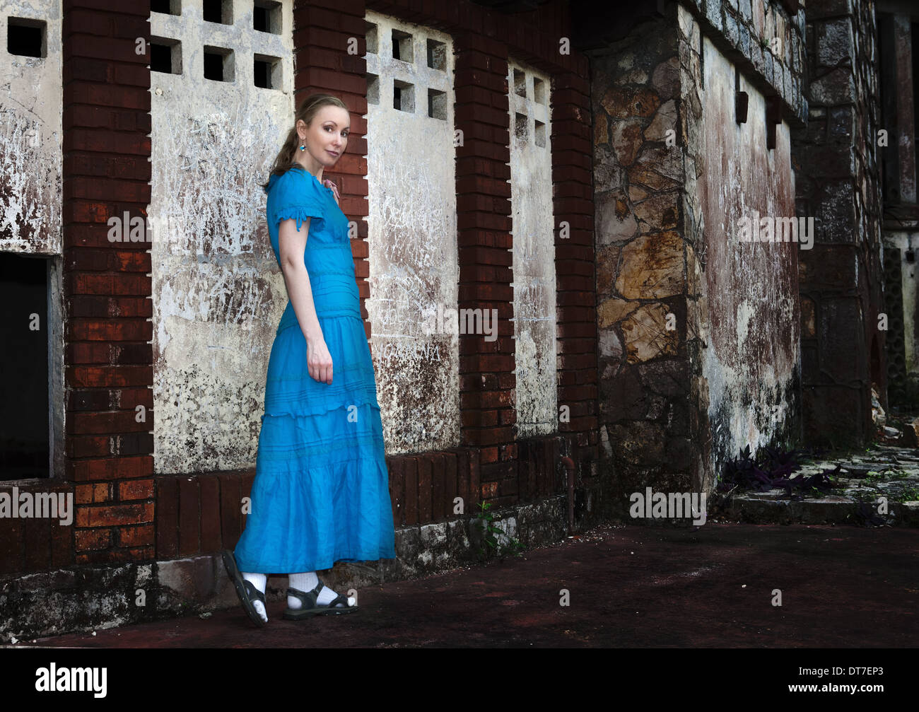 The young woman in a long blue dress stands near the old destroyed ...