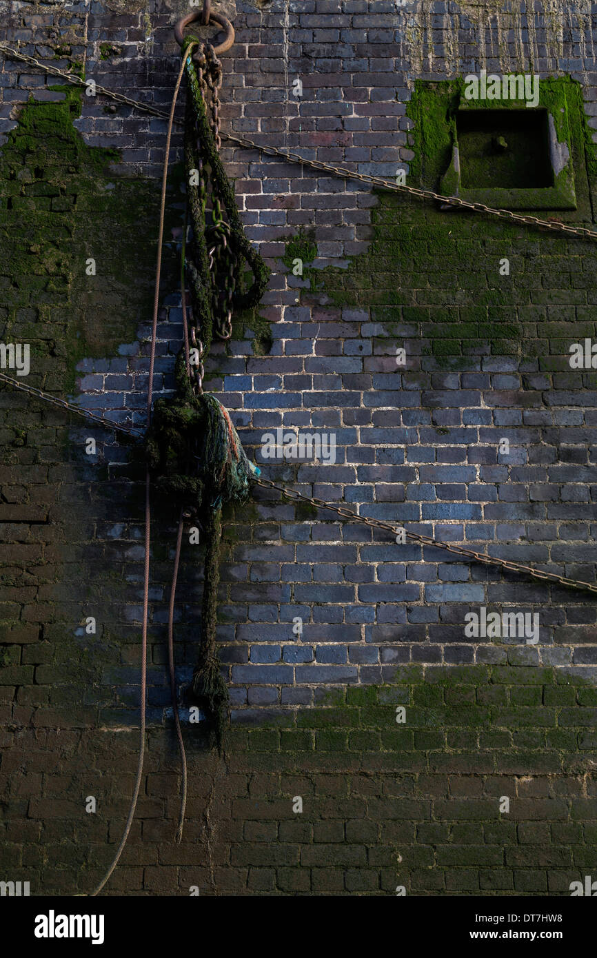 An old wall on the Thames foreshore with hanging chains and rope. Stock Photo