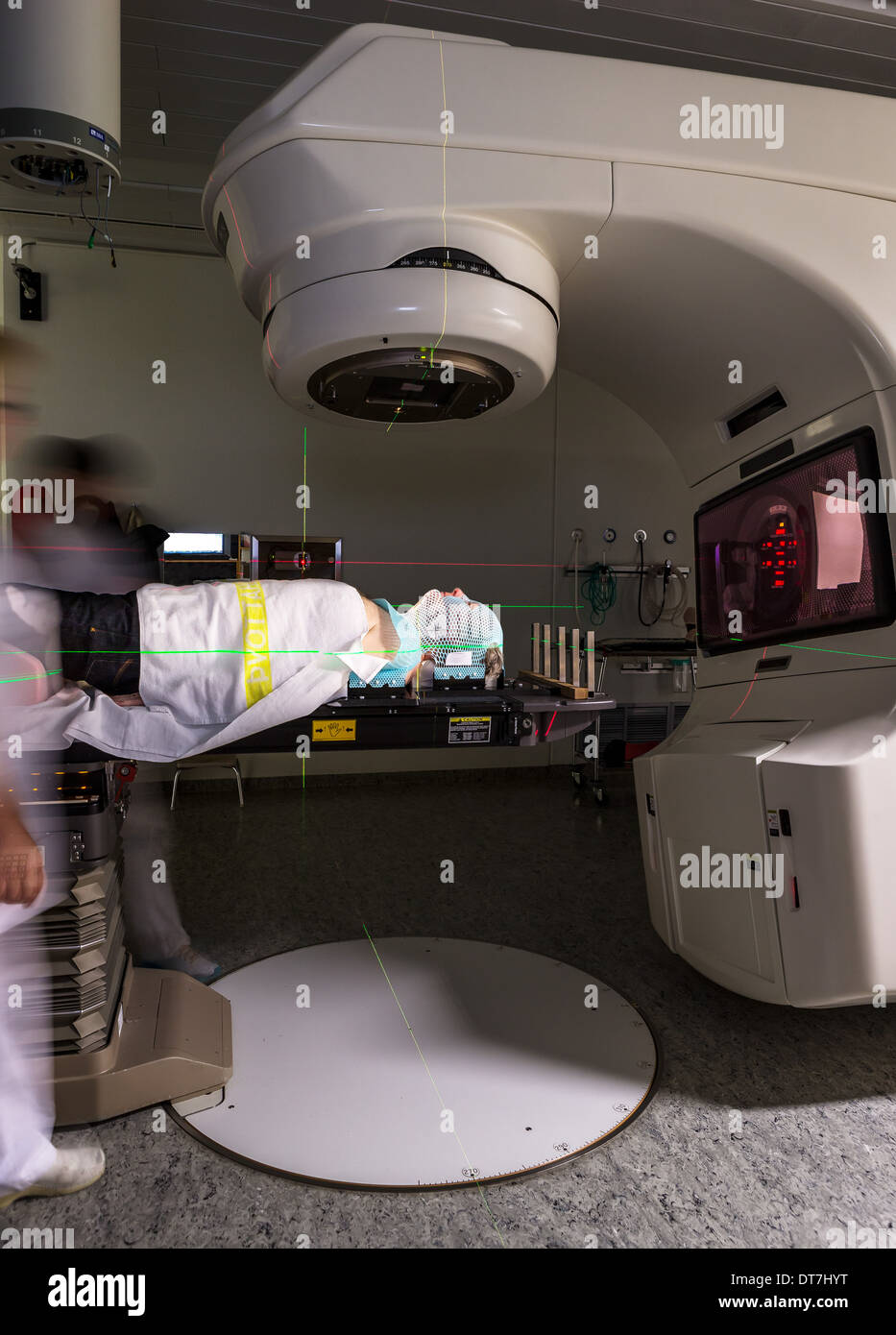 Male cancer under a linear accelerator or linac receiving radiation treatment.  Patient is wearing a plastic mesh mask. Stock Photo