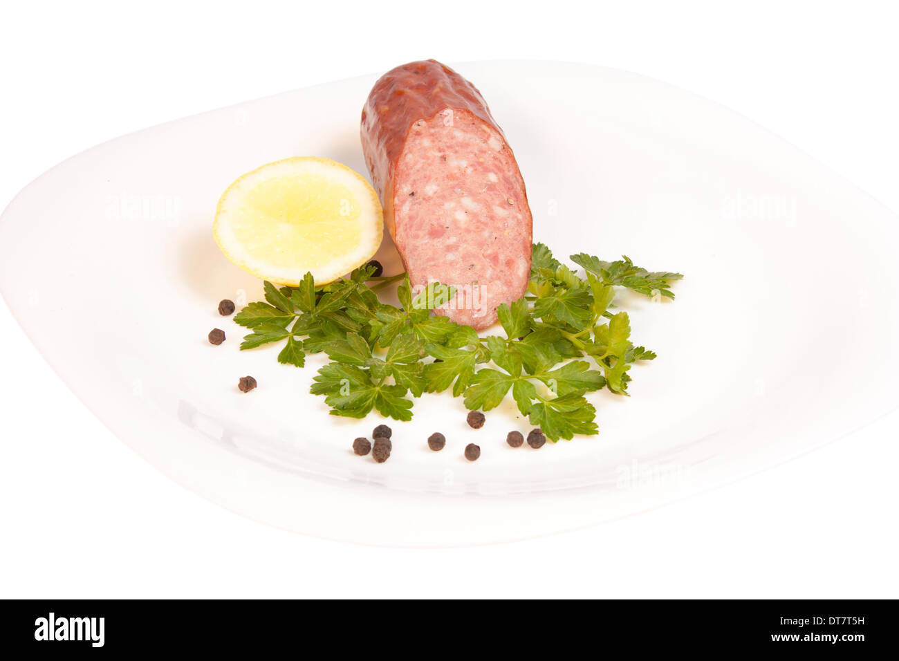 Salami with parsley, lemon and pepper on a plate isolated over white background with clipping path Stock Photo