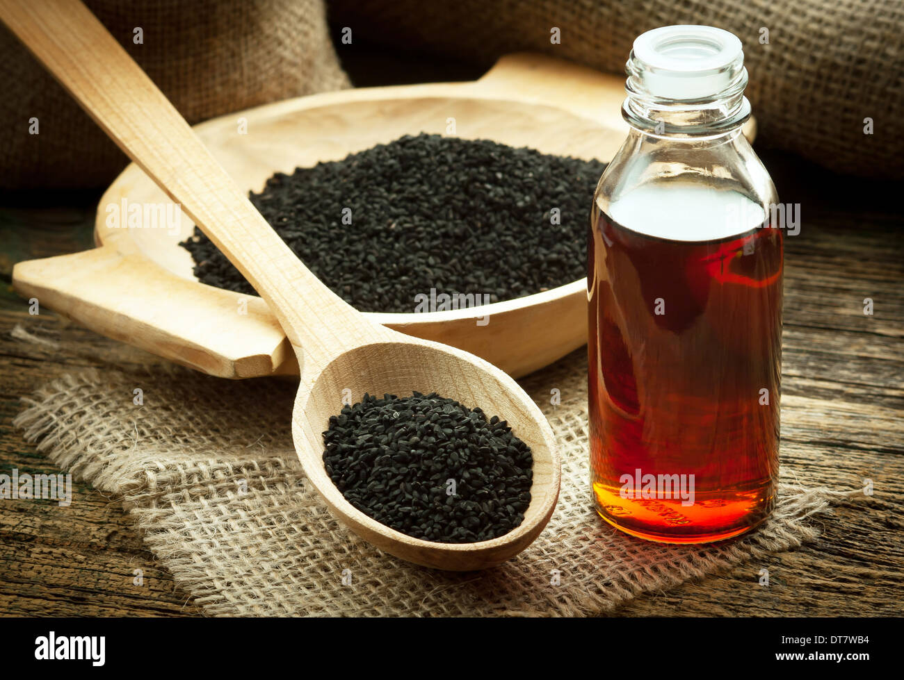 Nigella sativa (Black cumin) on wooden spoon and essential oil. Real oil from nigella looks like dark honey Stock Photo