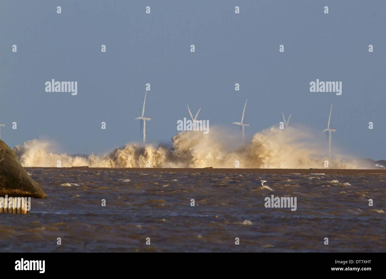 Waves crashing against remains of shingle sea defences with flooded marshes and partially submerged birdwatching hide after Stock Photo