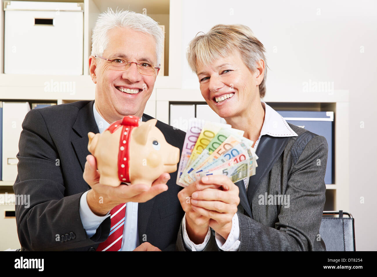 Two senior business people holding Euro money and piggy bank in the ...