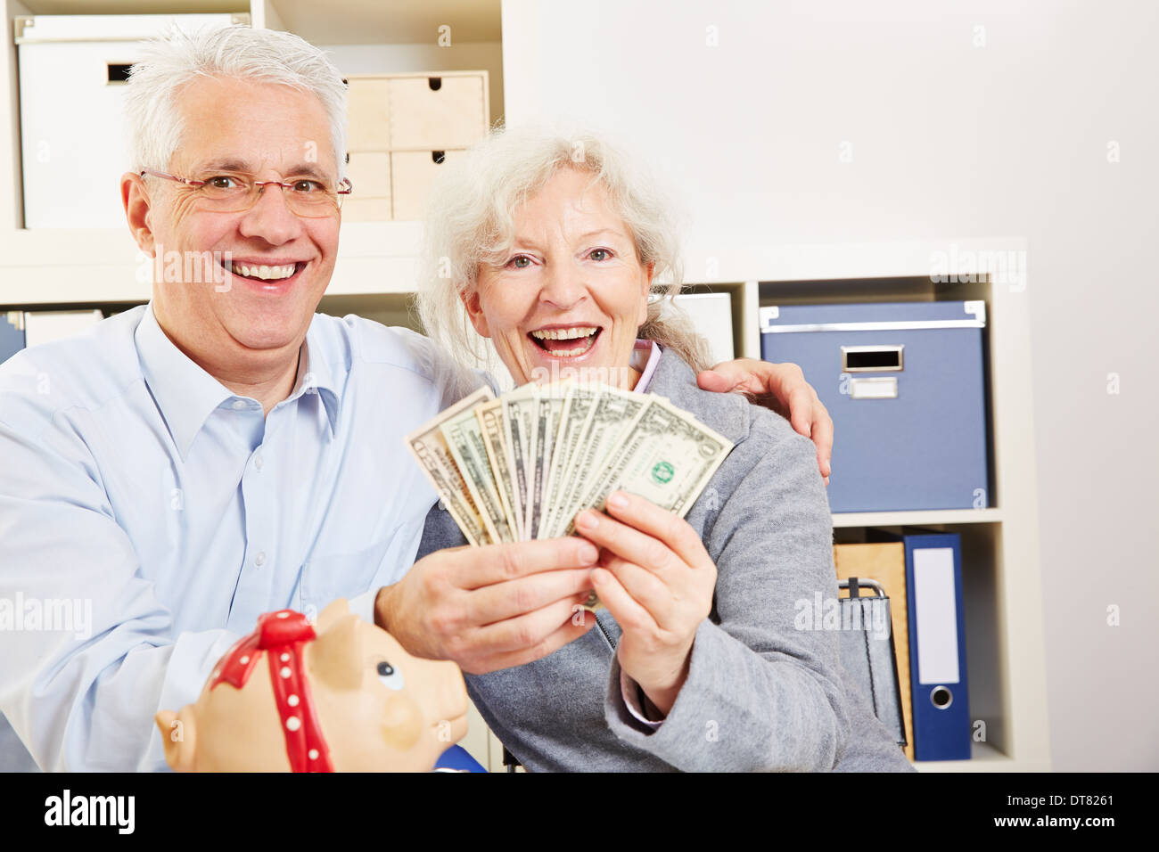 Happy senior couple with fan of dollar bills and a piggy bank Stock Photo