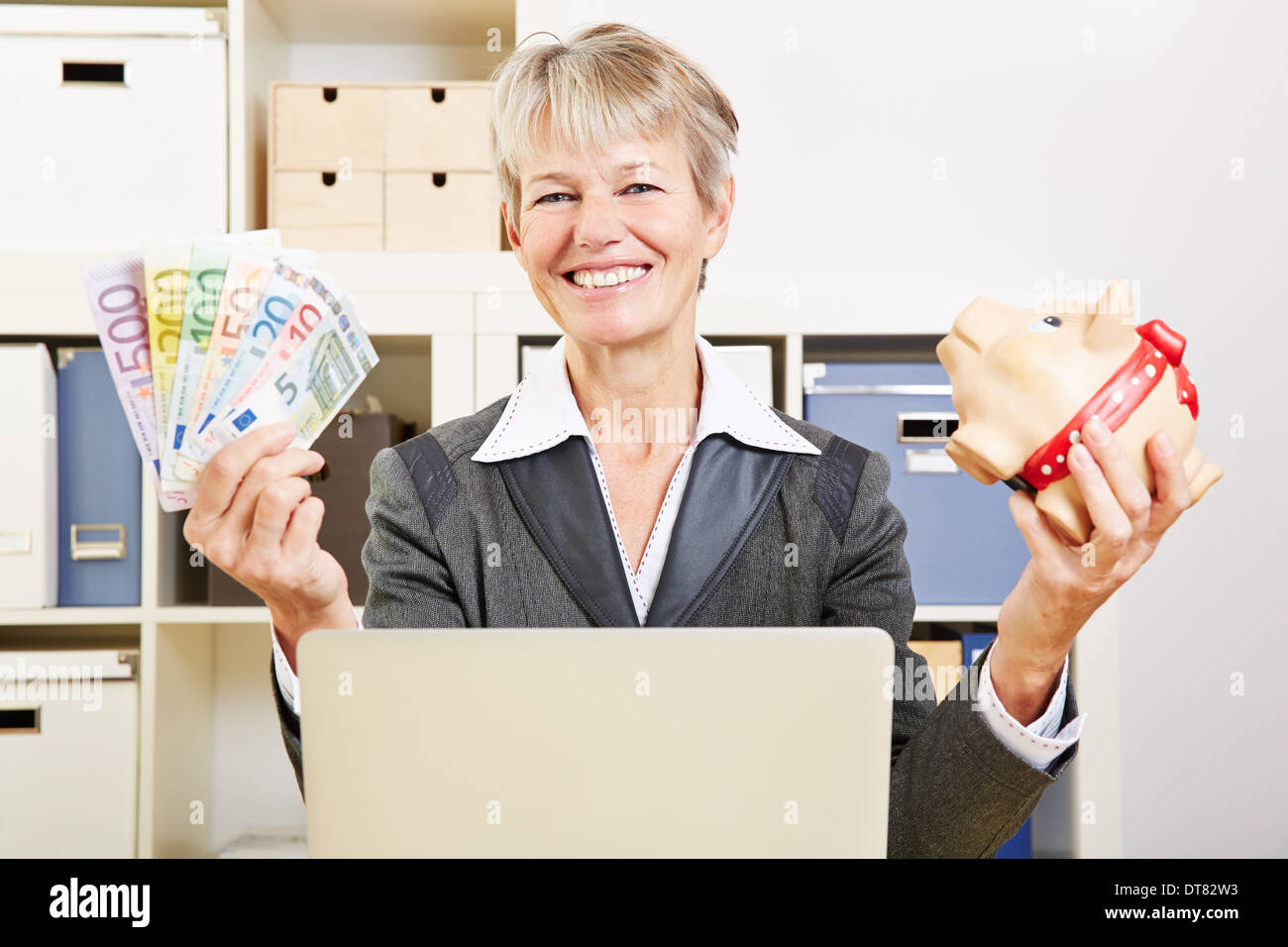 Happy senior business woman in her office with Euro money and a piggy ...
