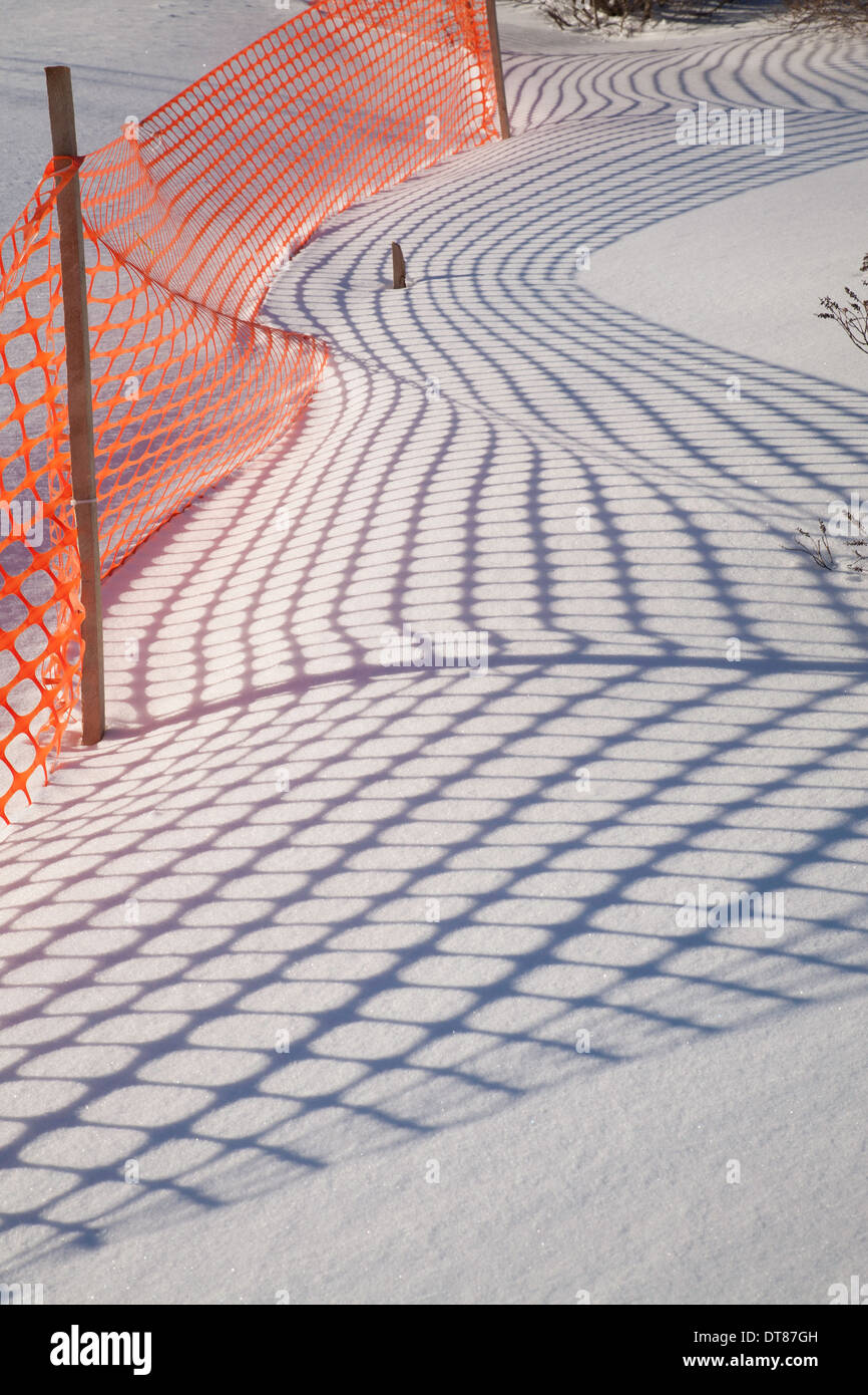 Shadows from an orange plastic snow fence make patterns on the New England snow. Stock Photo