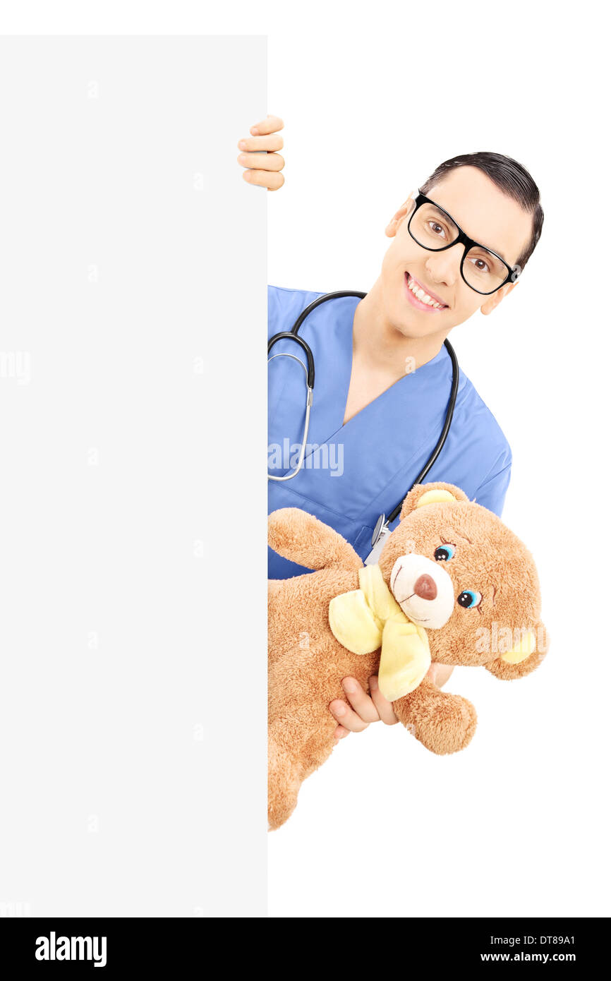 Young male nurse holding a teddy bear and peeking behind blank panel Stock Photo