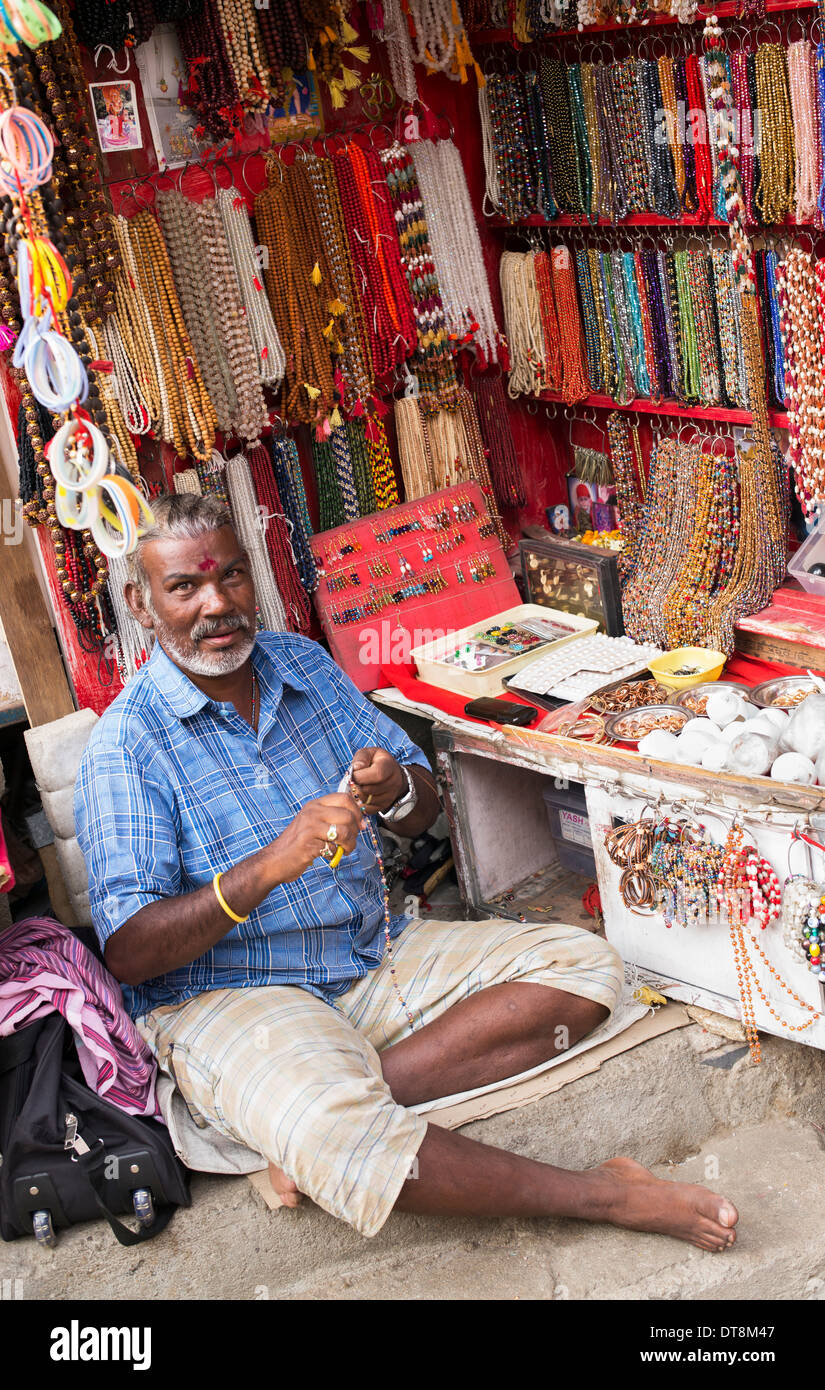 Indian man making necklaces and japamalas from an open street store. Puttaparthi, Andhra Pradesh, India Stock Photo