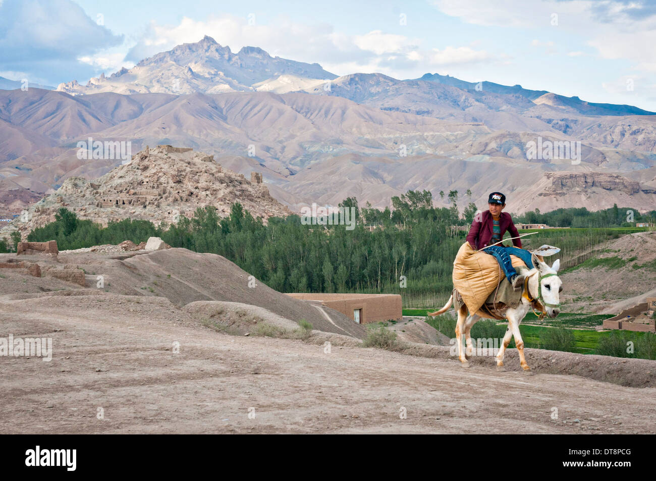 A young Afghan man rides a donkey through the countryside past the ruins of Shahr-e Gholghola, or the City of Screams June 24, 2012 in Bamyan, Afghanistan. Stock Photo