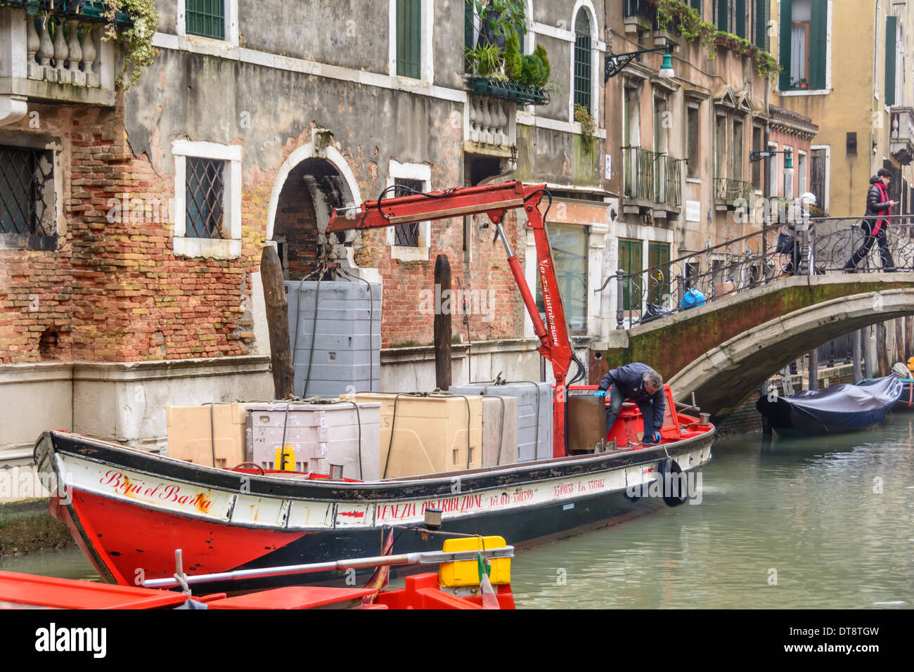 Venice, Italy. Freight-laden barge with mounted crane in a narrow Venetian canal unloading containers. Stock Photo
