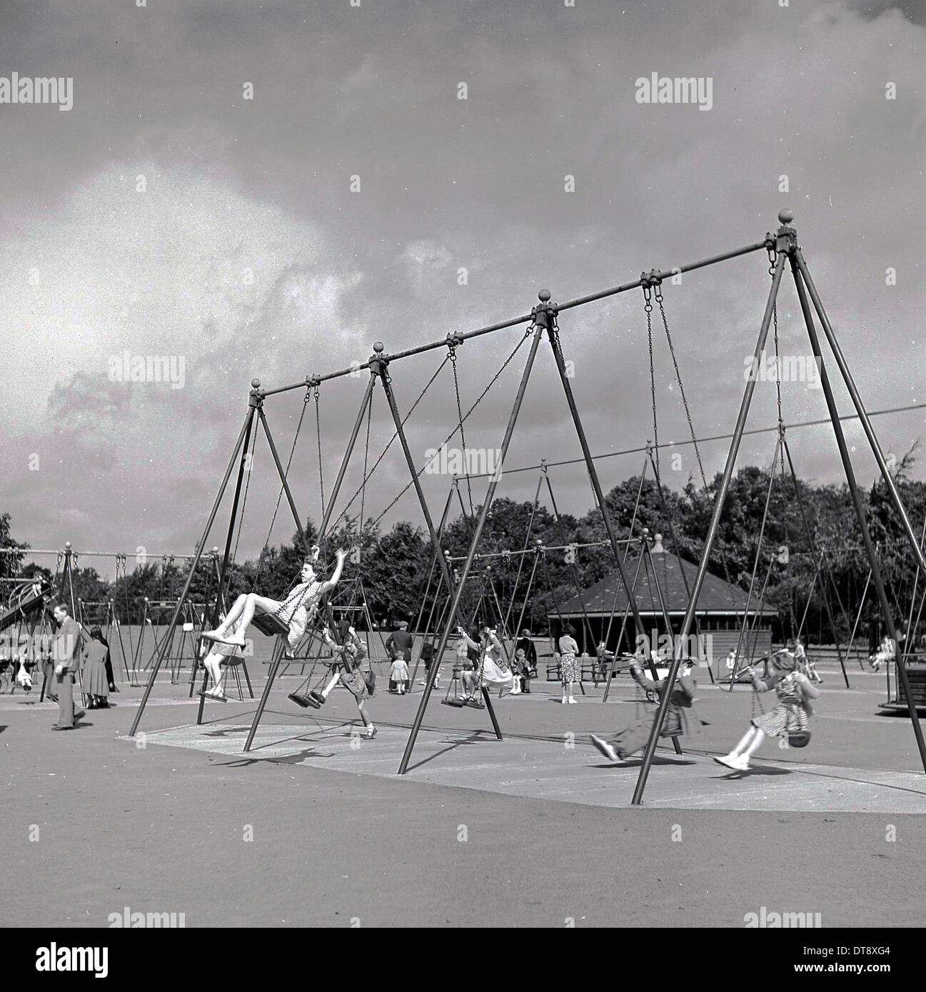 Historical picture from 1960s showing school children enjoying the traditional type swings in a recreational playground. Stock Photo