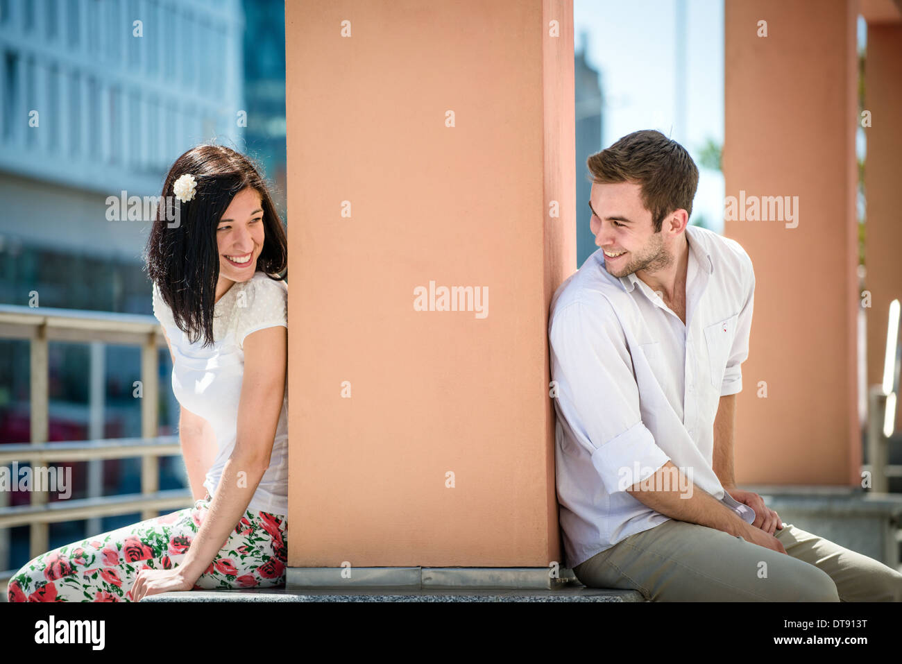 Two people sitting on opposite side of big collumn outdoor in street