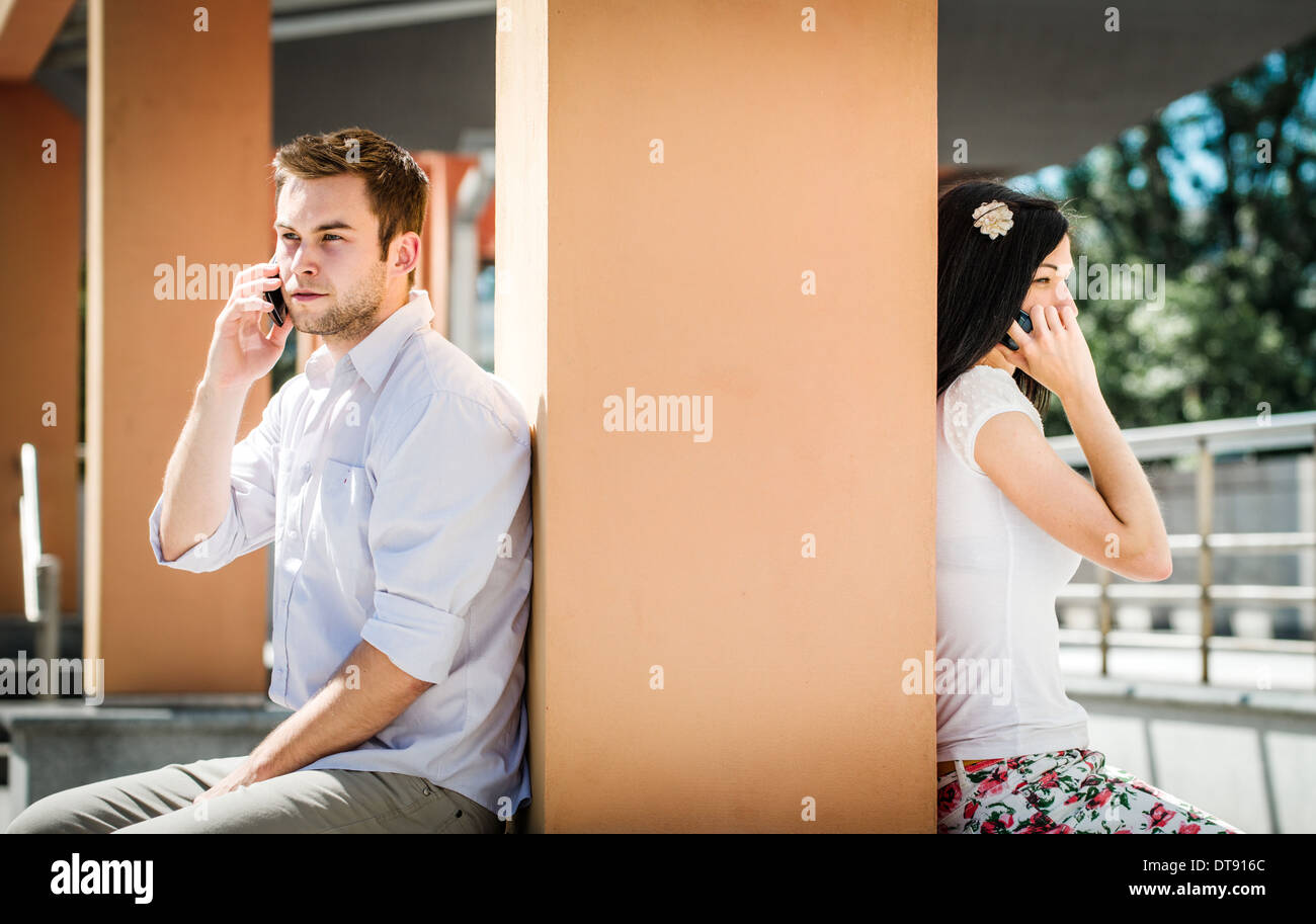 Couple having problems - two people sitting on opposite side of big collumn calling phone Stock Photo
