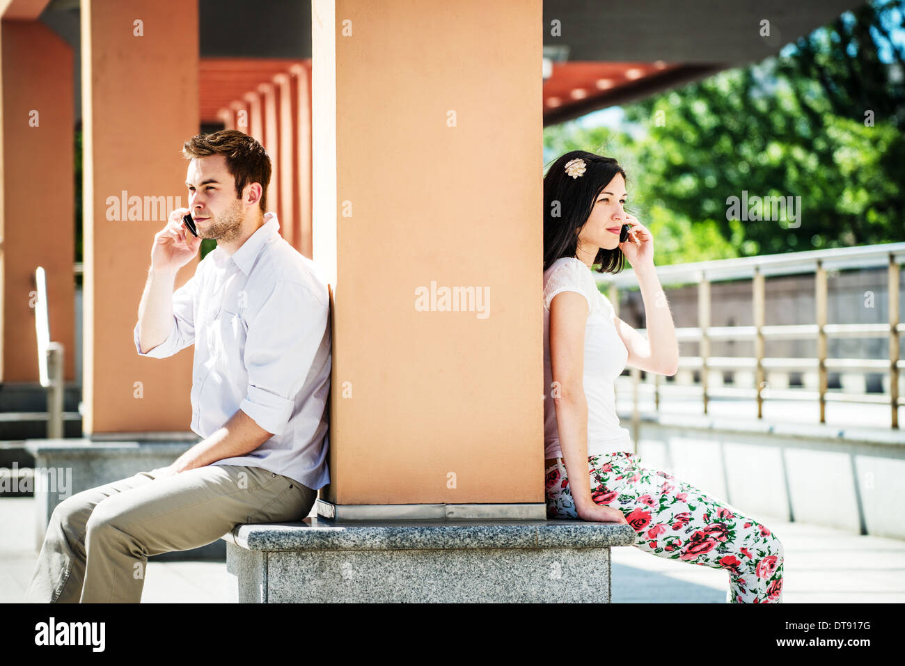 Couple having problems - two people sitting on opposite side of big collumn in street Stock Photo