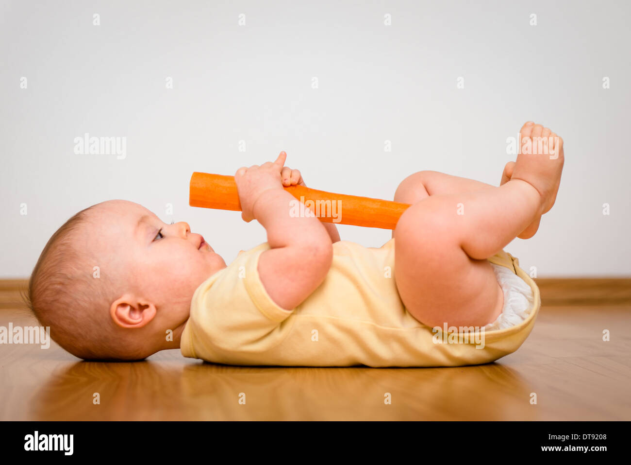 Baby exploring carrot indoors - healthy living Stock Photo