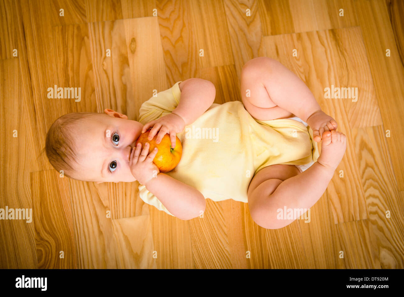 Baby eating apple lying on floor - from above Stock Photo