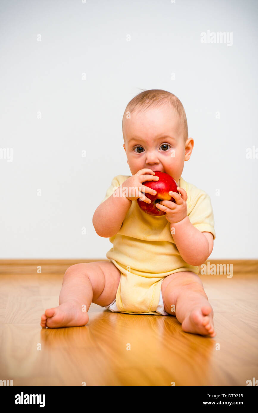 Baby eating apple lying on floor - healthy lifestyle Stock Photo
