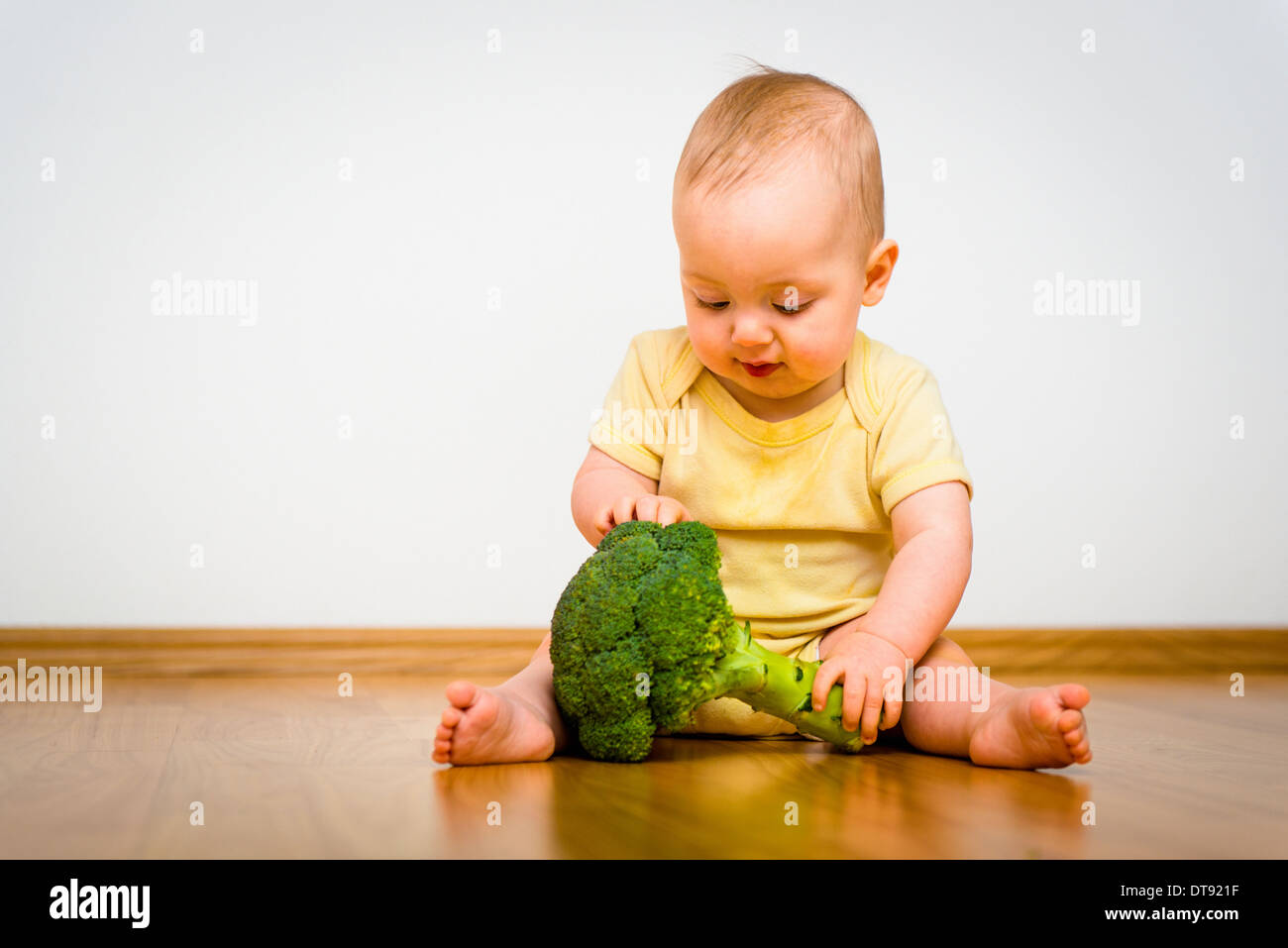 Cute baby exploring broccoli - sitting on floor indoors Stock Photo