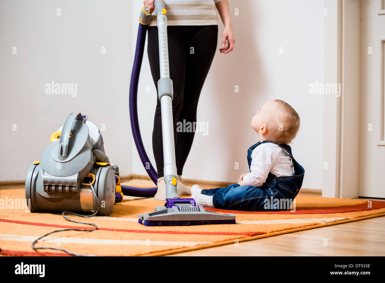 Cleaning up the room woman with vacuum cleaner, baby sitting on Stock