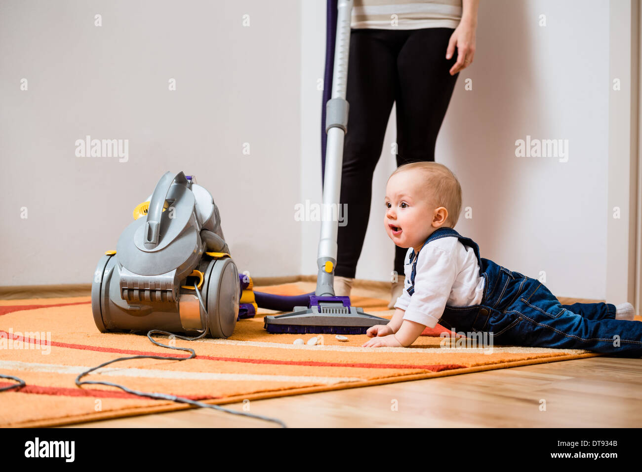 Cleaning up the room - woman with vacuum cleaner, baby sitting on floor Stock Photo
