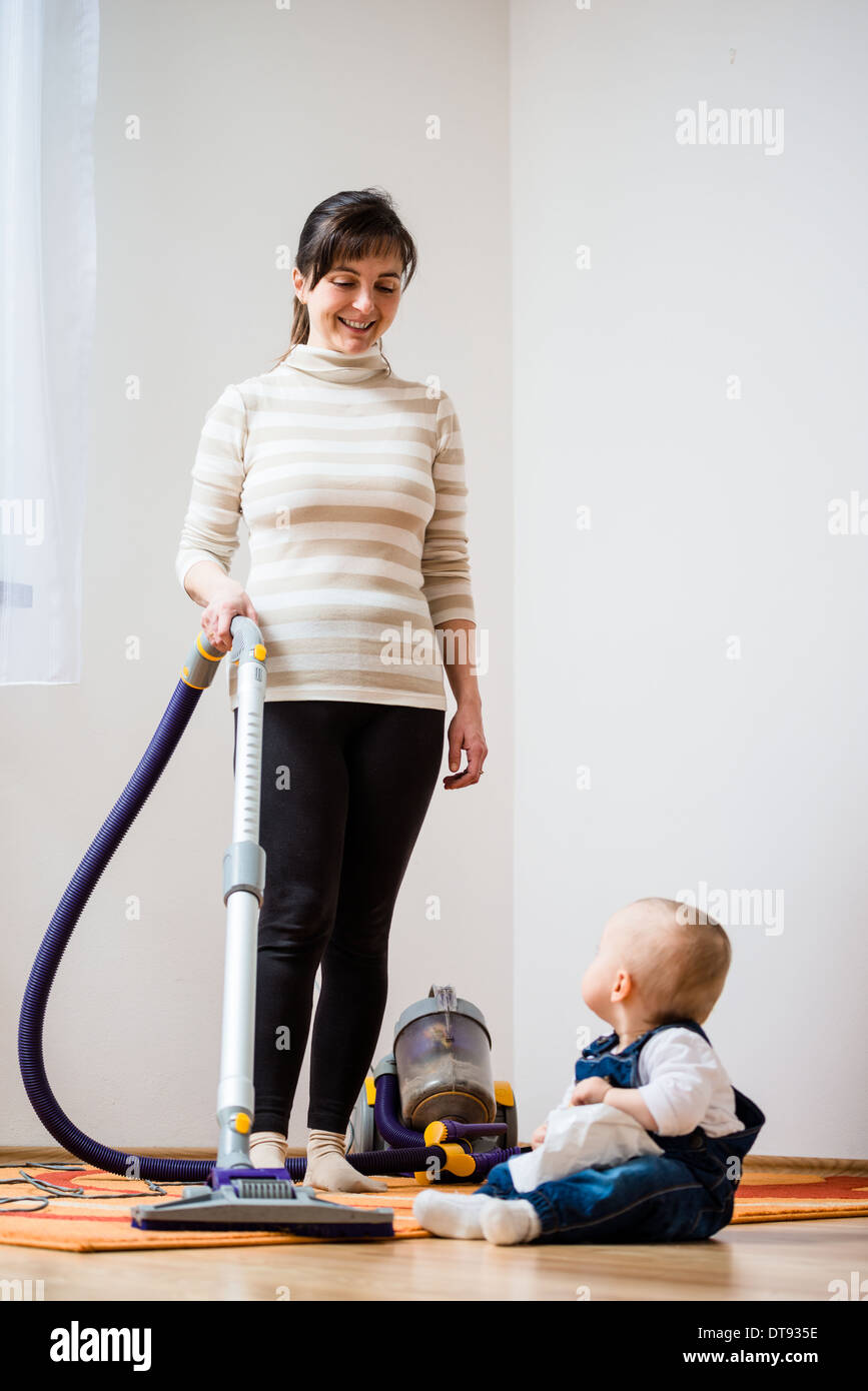 Cleaning up the room woman with vacuum cleaner, baby sitting on floor