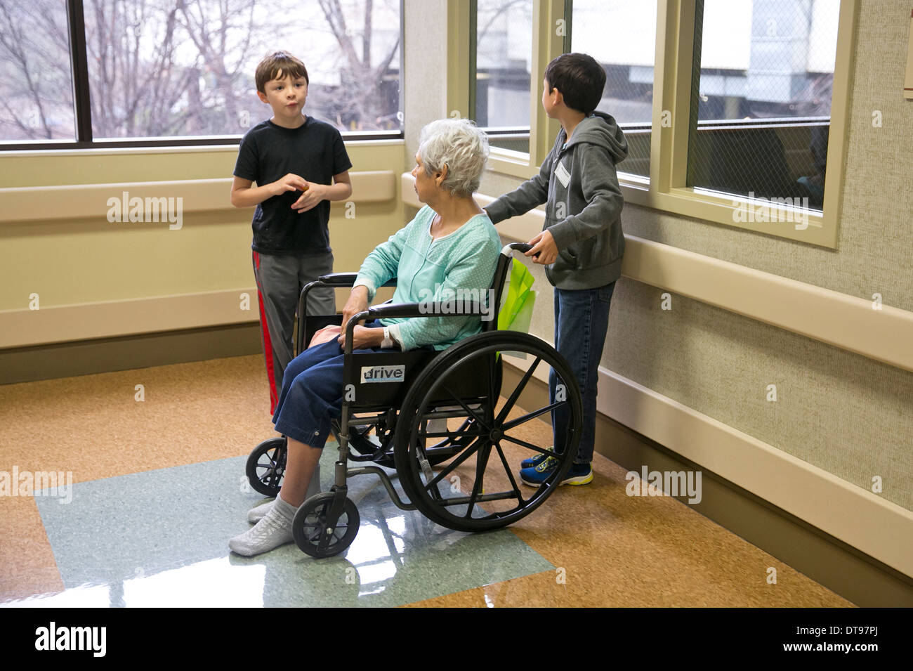 Grandsons visit with Hispanic elderly grandmother in a wheelchair at a rehabilitation hospital in Texas Stock Photo